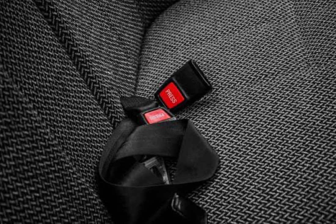 A dark textured car seat with a black seat belt buckle receiver set into it, photographed close up.