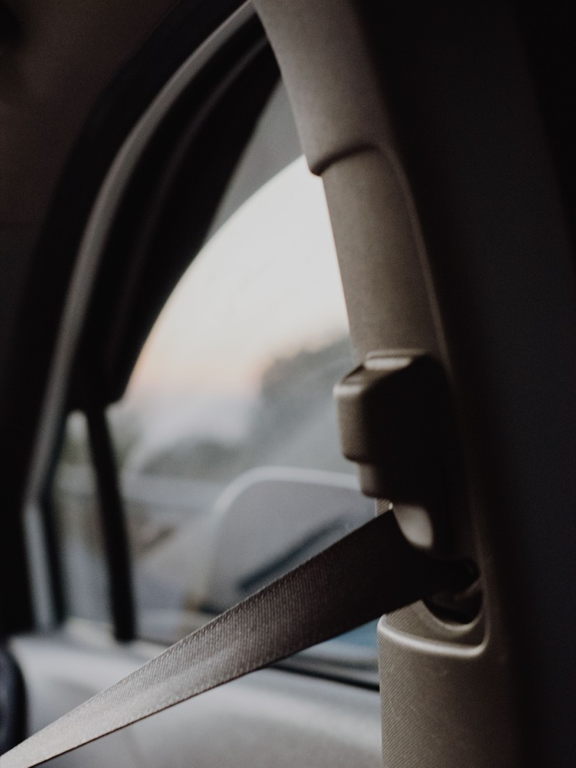 The upper anchorage point of a seat belt on a car B-pillar, with the webbing running down past the trim in soft daylight.