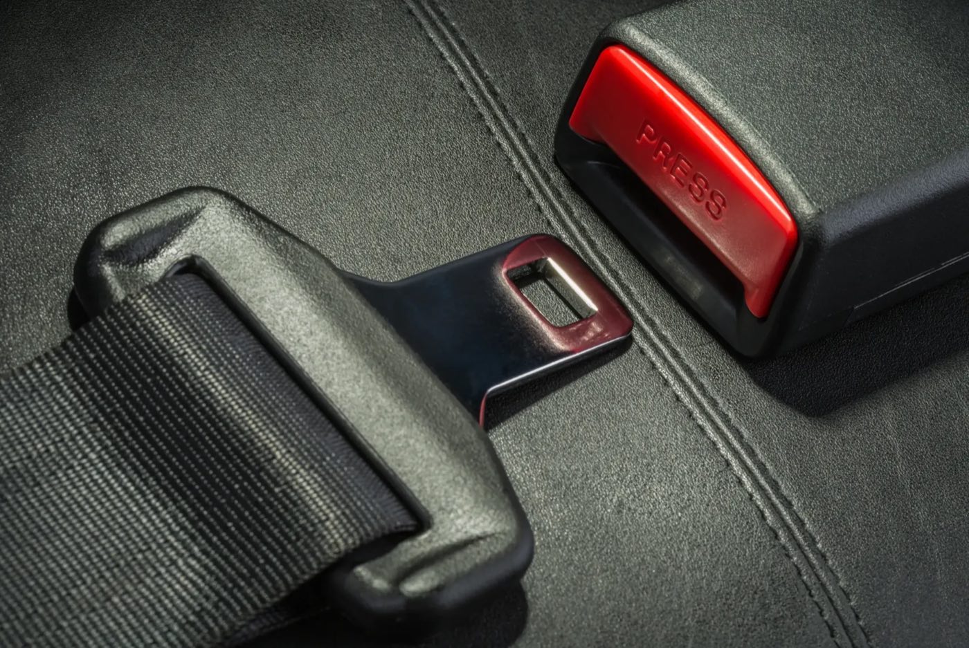 Close view of an automotive seat belt tongue resting beside its buckle receiver, with the red release button clearly visible.